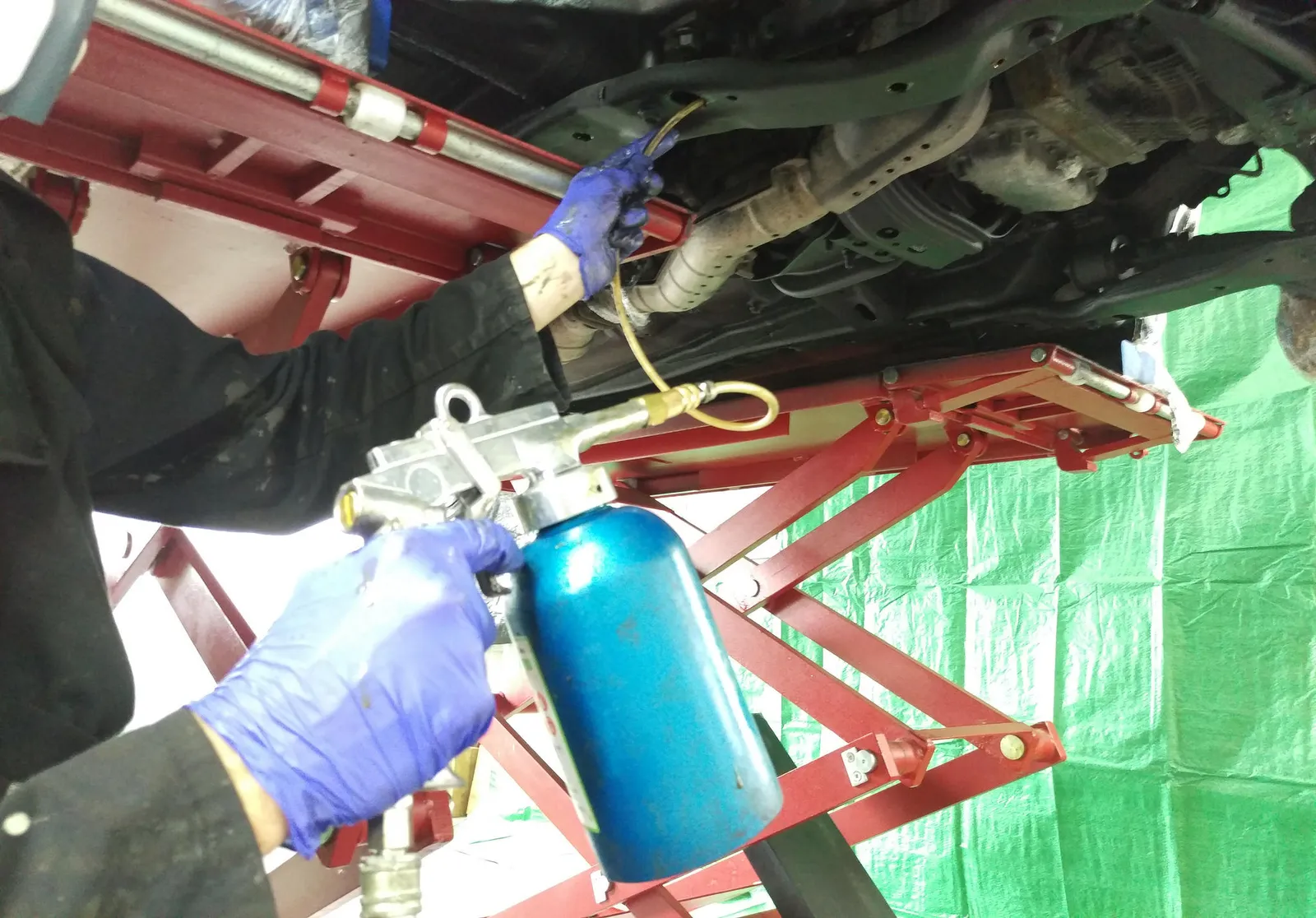 Mobile Rust Doctor technician injecting cavity wax inside a vehicle sill on a customer's driveway